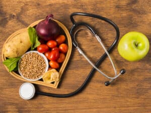 Das Bild zeigt verschiedene gesunde Lebensmittel auf einem Holztisch mit einem Stetoskop.