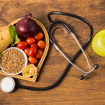 Das Bild zeigt verschiedene gesunde Lebensmittel auf einem Holztisch mit einem Stetoskop.