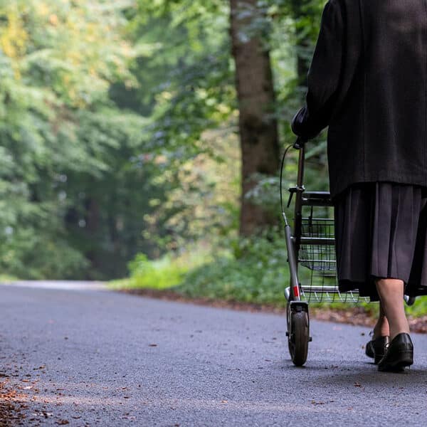 Das Bild zeigt eine ältere Frau mit einem Rollator spazieren.