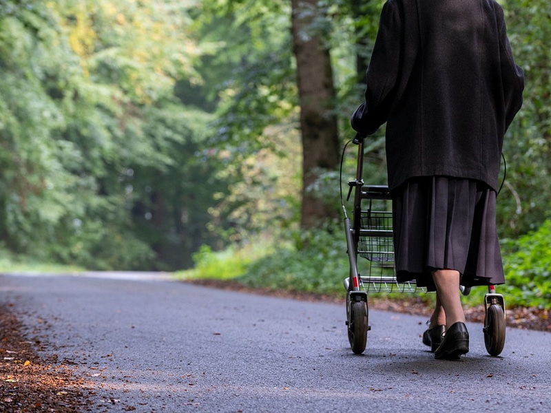 Das Bild zeigt eine ältere Frau mit einem Rollator spazieren.
