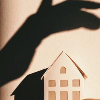 Der Schatten einer Hand ist an der Wand über einem Papierhaus abgebildet.