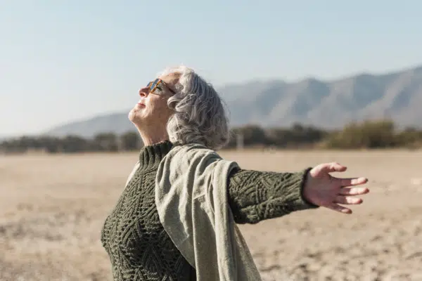 Das Bild zeigt eine Frau am Strand, welche sich Richtung Sonne streckt.